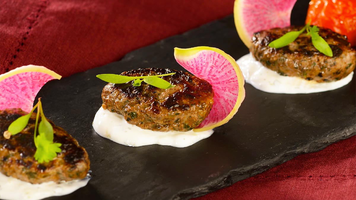 close up of dish with patties over sauce with garnishes on black ceramic slab on table with red cloth at Spice Road Table Food (Morocco) at Epcot in Orlando, Florida, USA